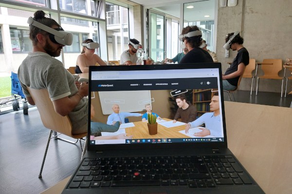 Das Bild zeigt eine Gruppe von Personen im Stuhlkreis. Alle haben eine VR-Brille auf. Davor ist ein aufgeklappter Laptop, der ein VR-Szenario auf dem Bildschirm zeigt.