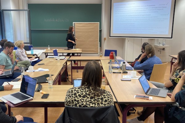 Mehrere Personen sitzen in einem Seminarraum. Vorne wird eine Präsentation gezeigt.